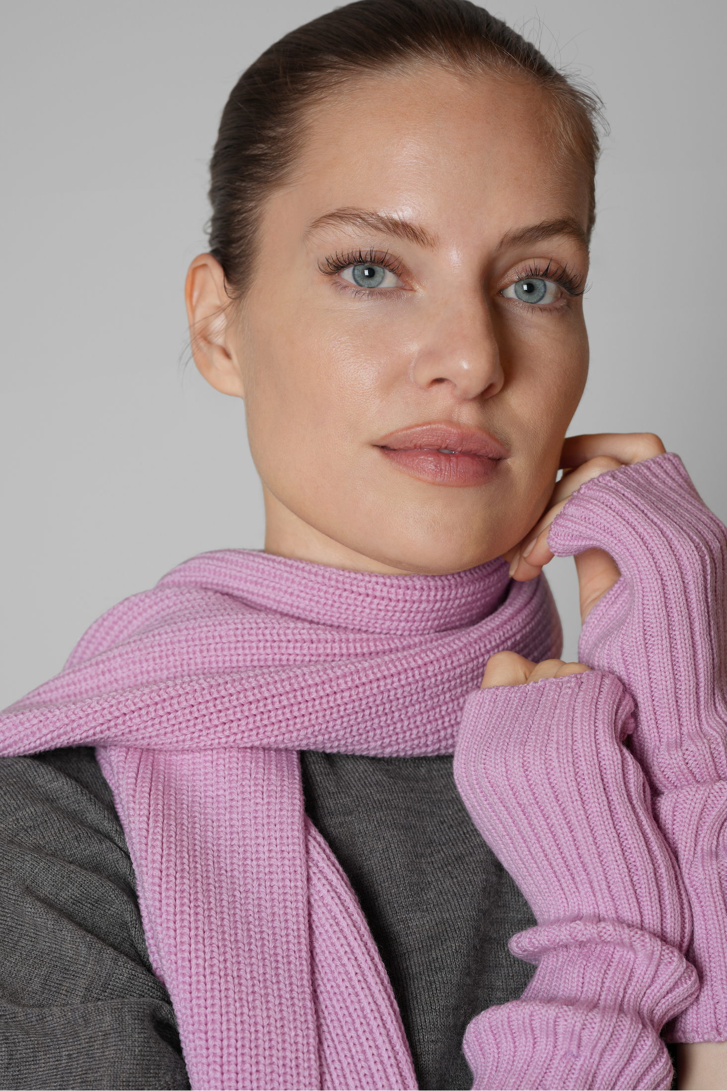Woman wearing a pink scarf and gloves against a gray background