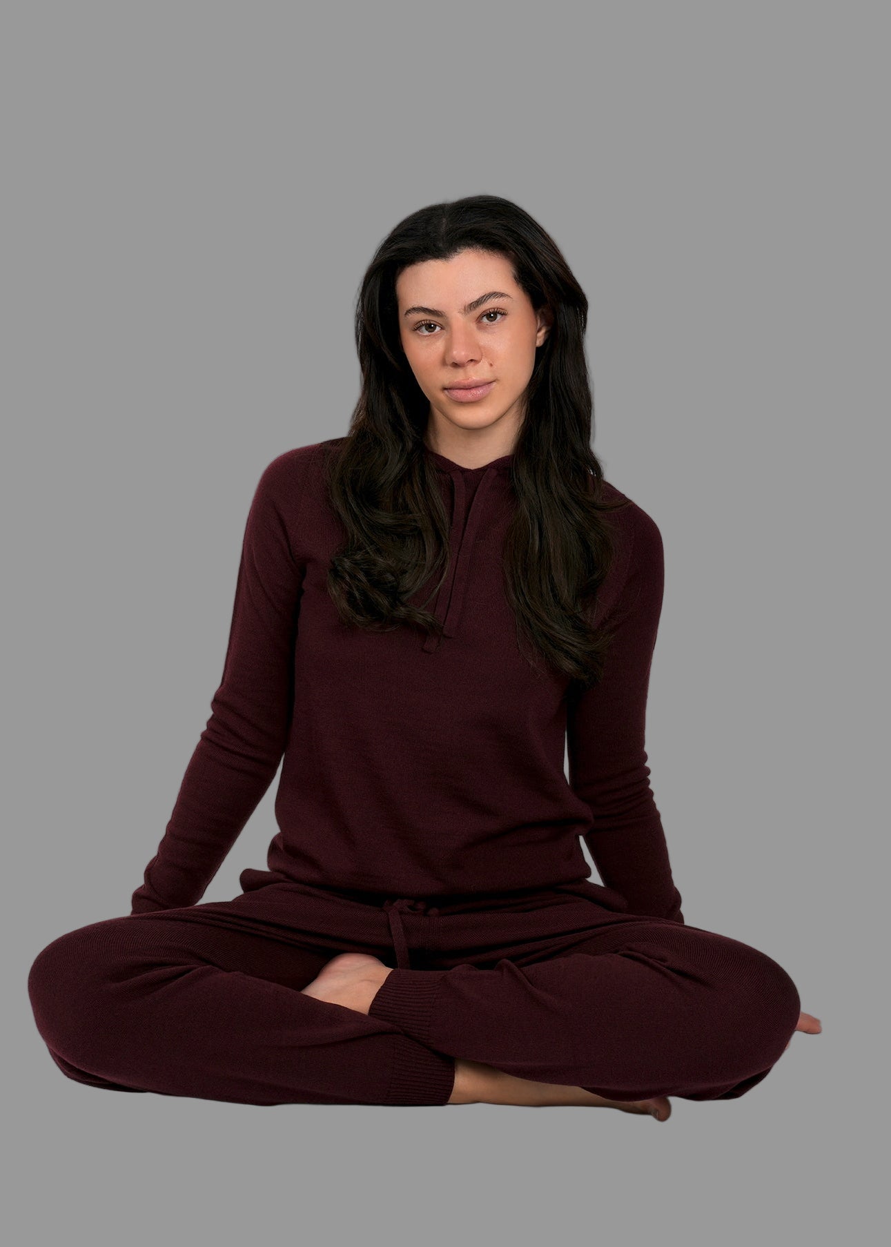 Woman wearing a burgundy outfit sitting in a lotus position on a gray background