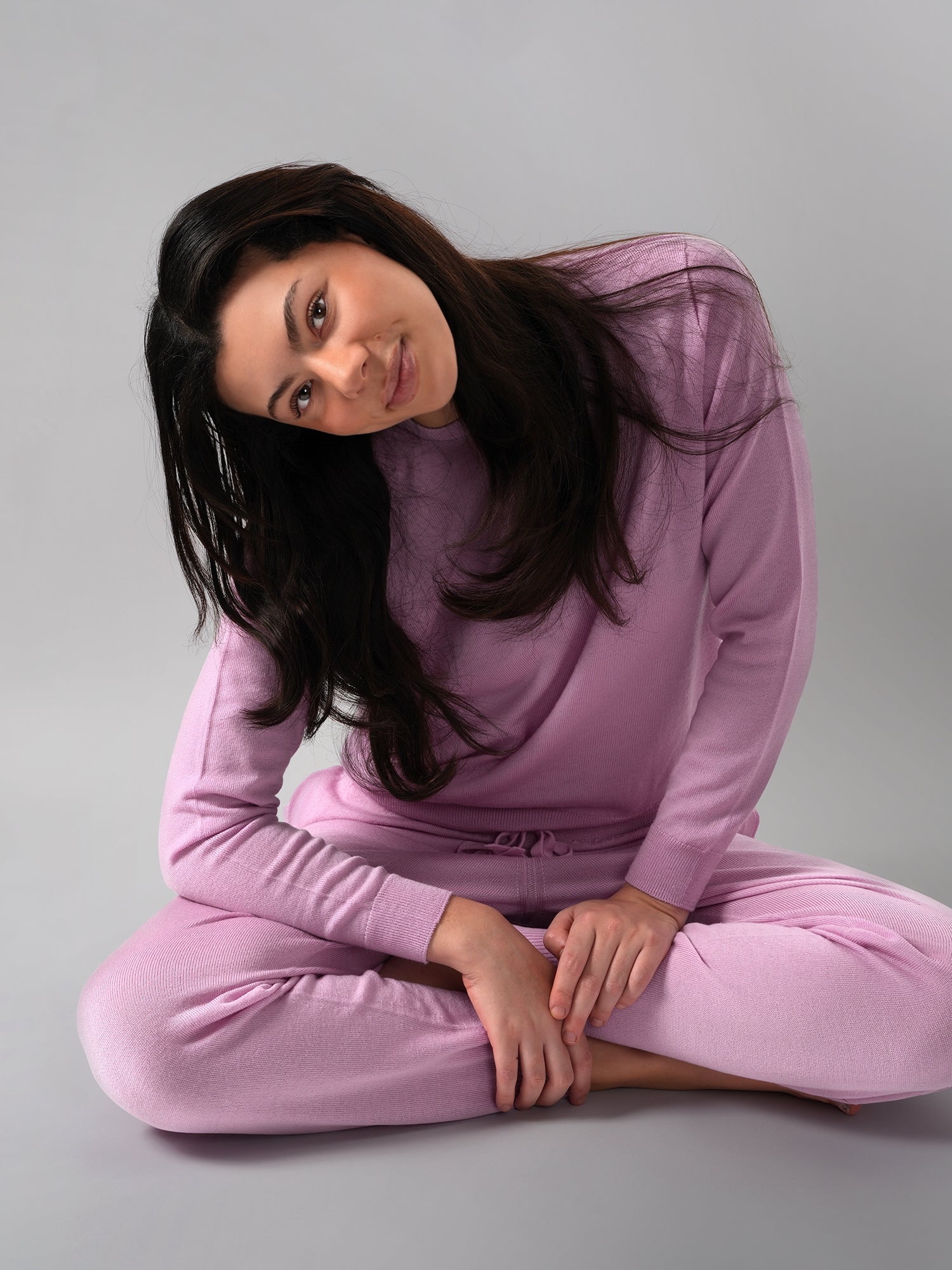 Woman wearing a pink pajama set sitting on a gray background