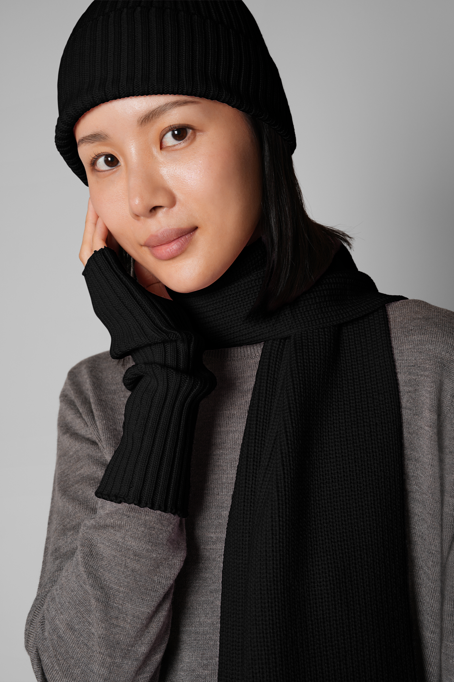 Person wearing a black knit hat and scarf against a gray background