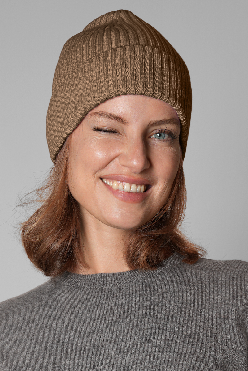 Woman wearing a brown knit beanie against a gray background