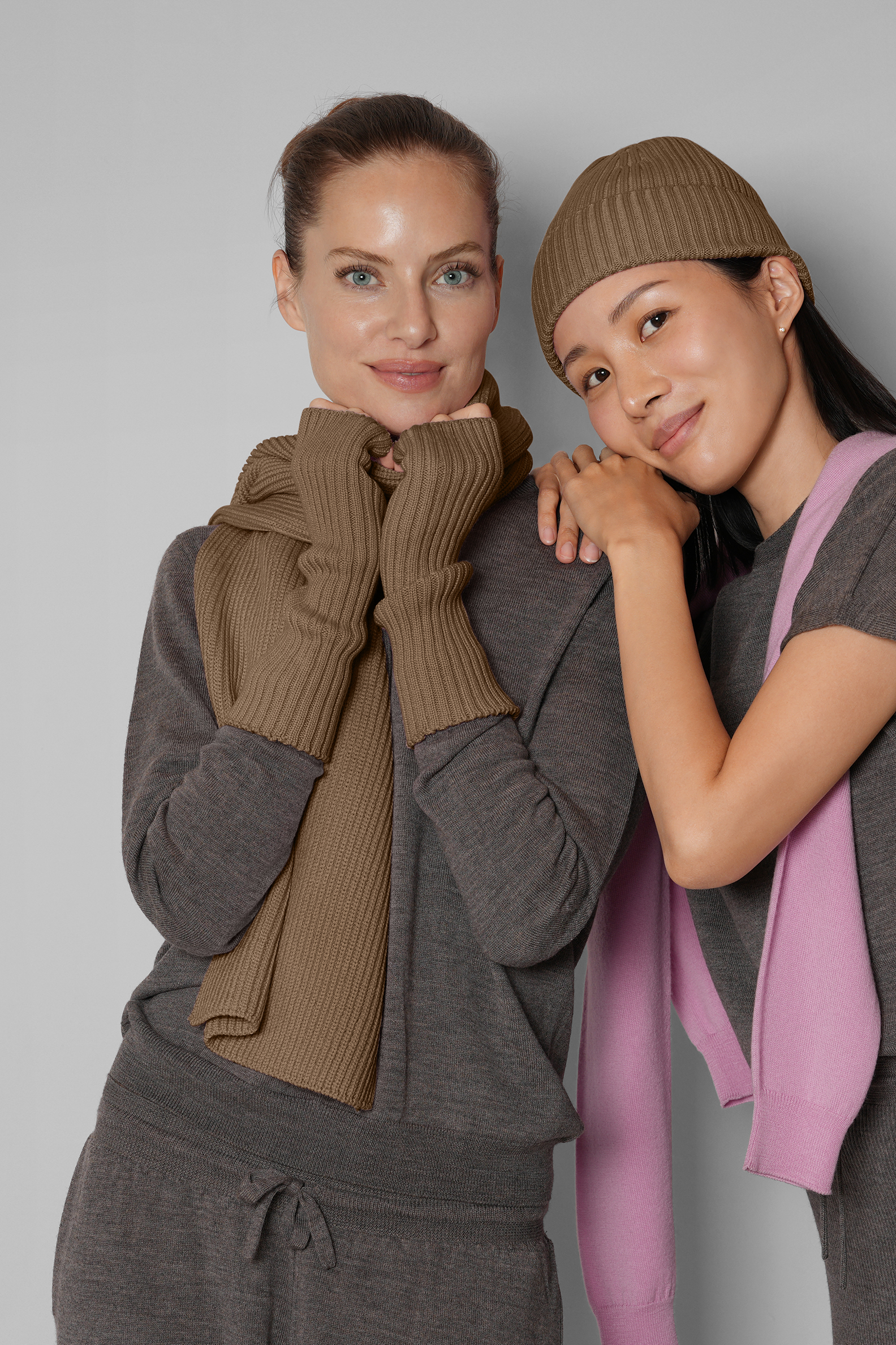 Two women wearing matching brown and gray outfits with scarves against a plain background