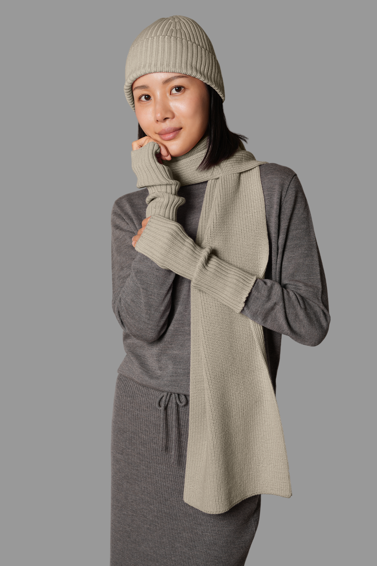 Person wearing a gray outfit with a matching beanie and scarf against a gray background
