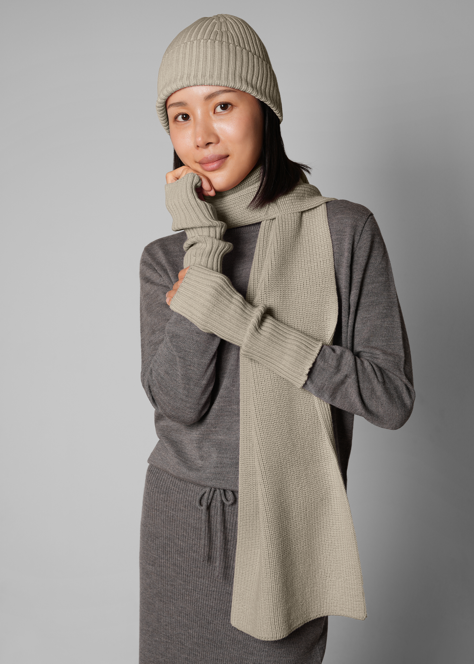 Person wearing a gray outfit with a matching beanie and scarf against a gray background
