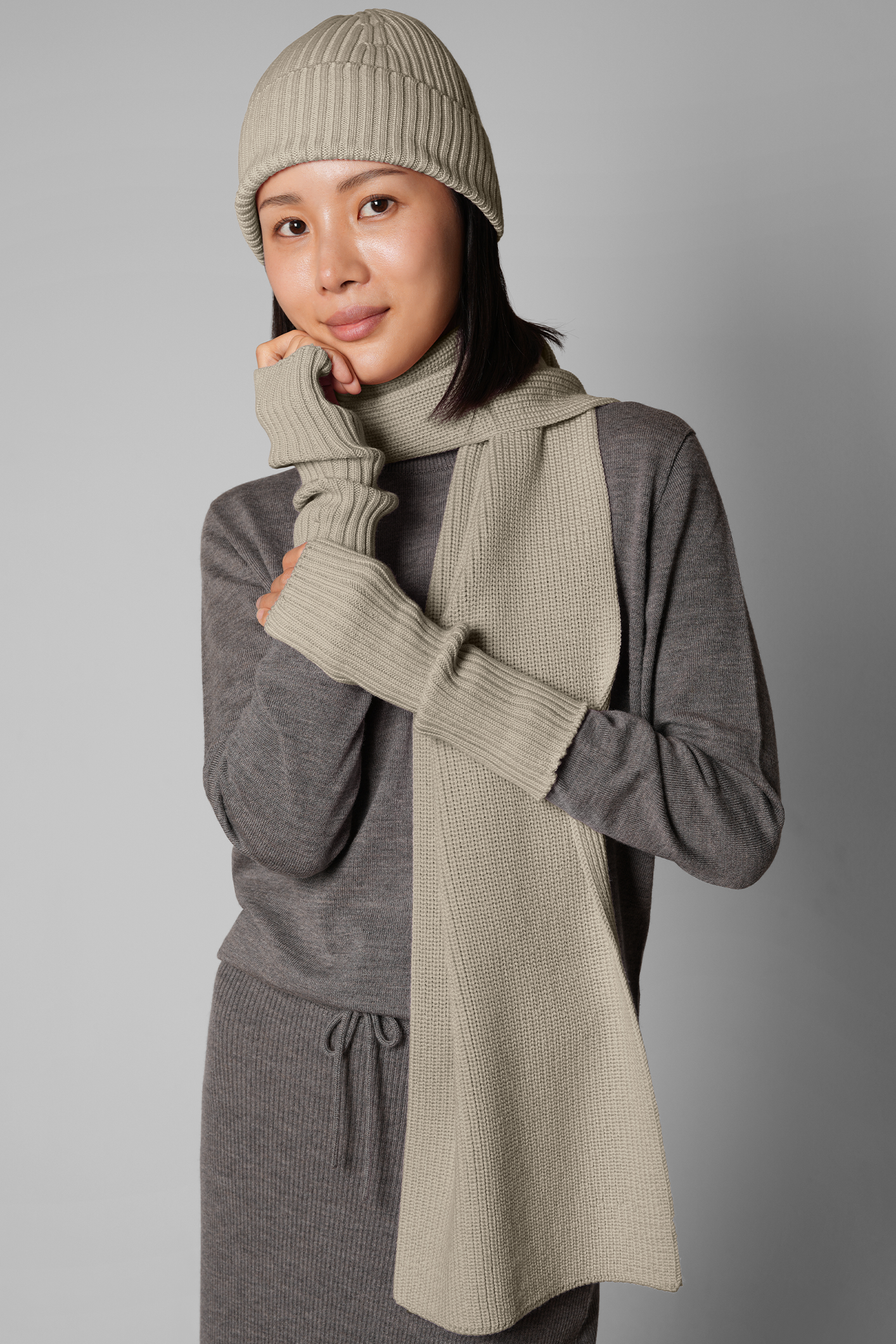Person wearing a gray outfit with a matching beanie and scarf against a gray background